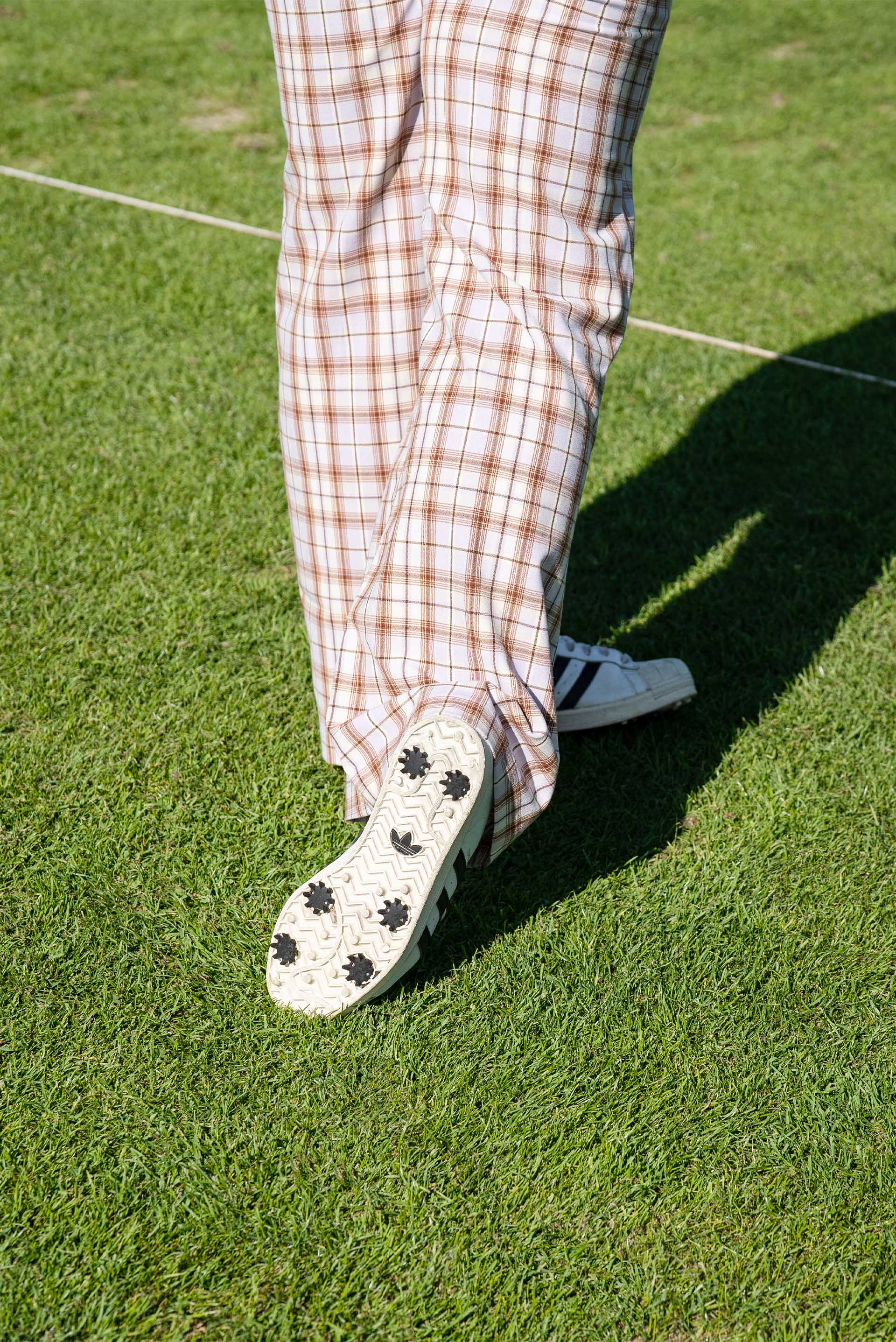 Detail van de geruite golfbroek en sneakers die Mullins op de baan draagt.